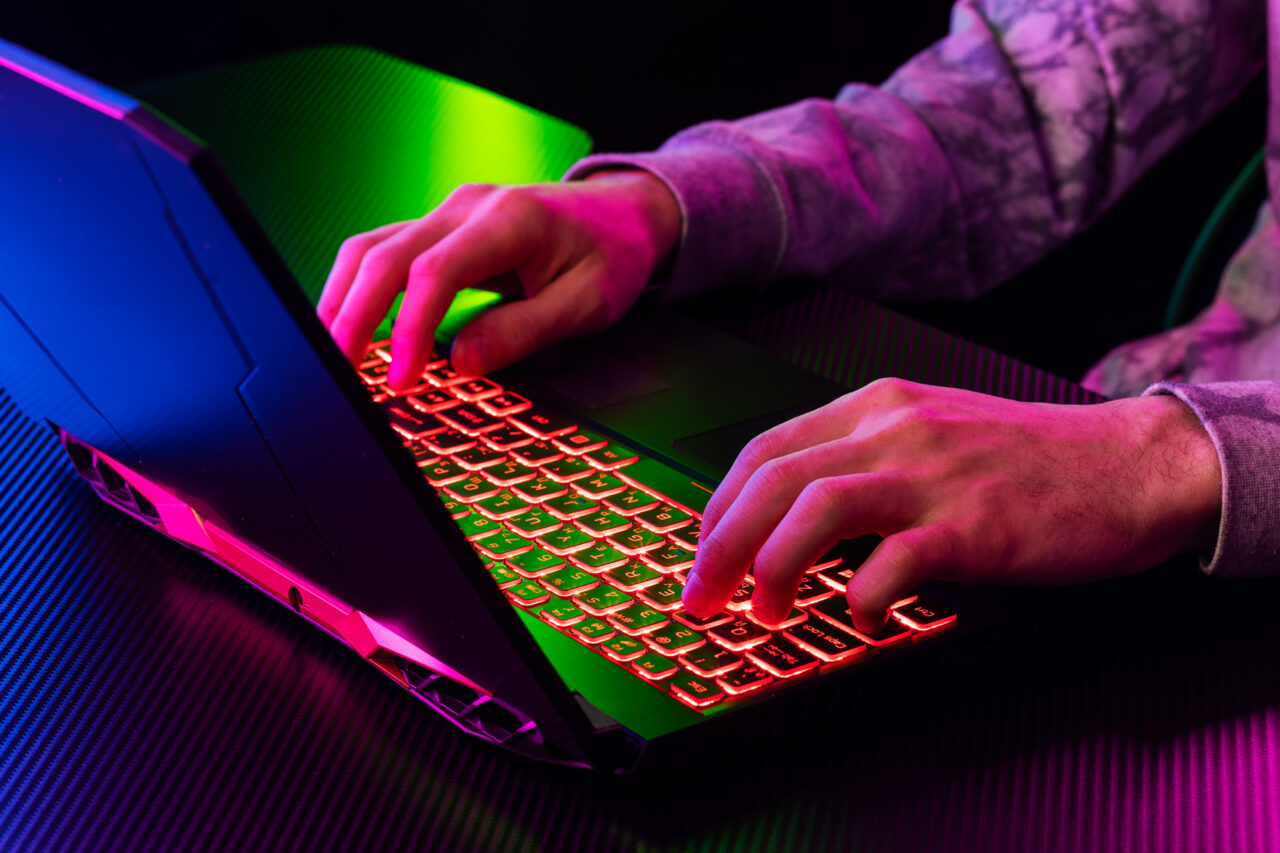 Hands typing on RGB gaming laptop keyboard in neon light