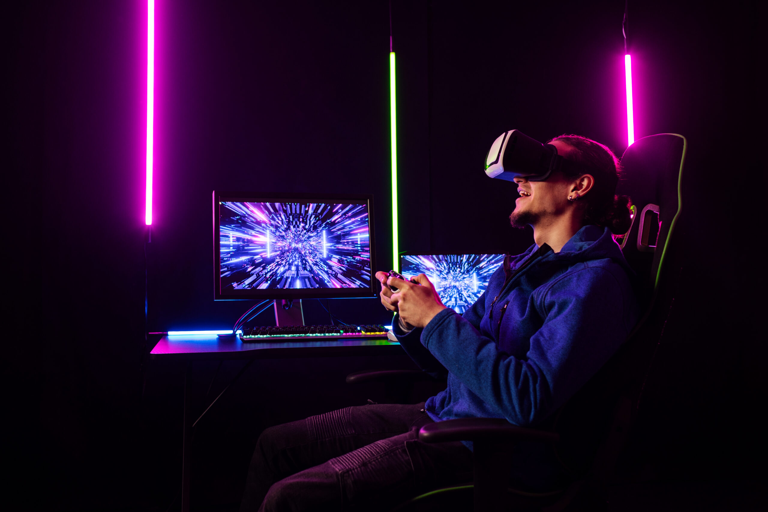 Man with VR headset playing video games in a neon-lit room, gaming monitor with colorful effects, purple and pink neon lights
